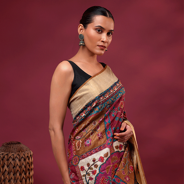 A model showcasing a royal plum unstitched pure Tussar silk saree with intricate hand-embroidered multi-colour Kantha floral patterns and a classic gold zari border.