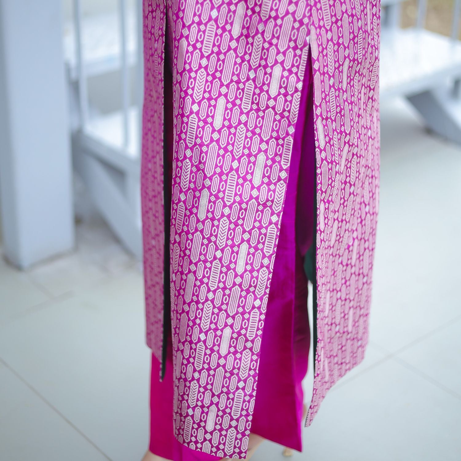 Close-up view of a royal purple handwoven brocade achkan suit, highlighting the intricate gold woven pattern and the elegant deep green silk lining visible through the side slit.