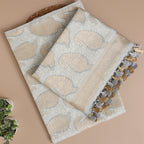 A flat-lay view of a luxurious silver-grey Banarasi silk suit fabric featuring intricate gold paisley motifs, a soft woven texture, and elegant tassel detailing on the dupatta edges.
