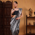 A model showcasing a white and silver pure katan silk Banarasi saree with an intricate Shikargah pattern and Zari Jaal weave, paired with a black blouse.