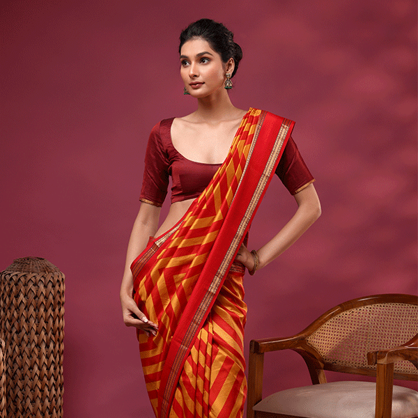 A model posing in the Sunlit Symphony pure Banarasi silk saree featuring radiant yellow and red all-over handwoven stripes, paired with a solid dark red silk blouse.