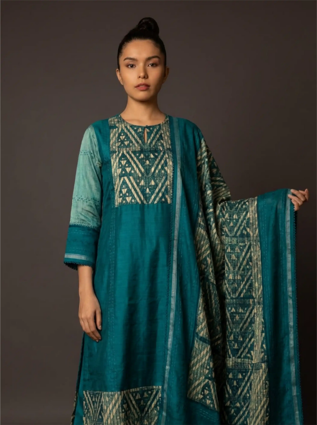 Woman wearing a teal traditional kurta set with a printed geometric pattern and matching dupatta against a dark background