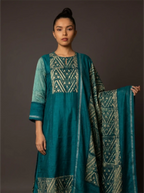 Woman wearing a teal traditional kurta set with a printed geometric pattern and matching dupatta against a dark background