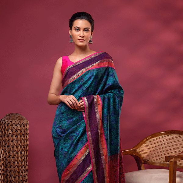 A model posing in a premium pure Banarasi silk saree featuring abstract digital prints in serene twilight blue and green shades, paired with a vibrant pink sleeveless blouse.