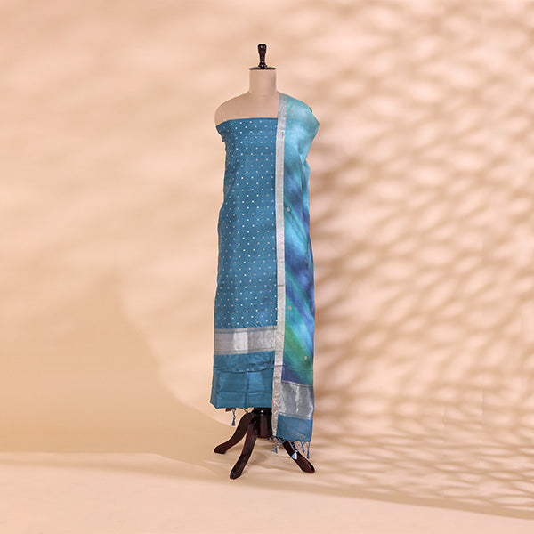 Handwoven turquoise tie and dye silk unstitched suit displayed on a mannequin, featuring shiny silver work on the body and an elegant blue and green ombre dupatta.