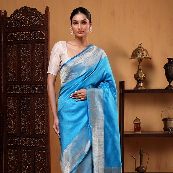A model posing in a luxurious oceanic azure pure tissue silk Jamdani saree featuring intricate gold and silver double weave Zari detailing.