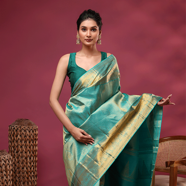 A model posing in a handwoven green and blue two-cross color Kanjivaram silk saree featuring a luxurious heavy gold zari pallu and a sleeveless green blouse.