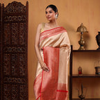 Full-length view of a woman posing in a White Opulence Banarasi Silk Saree, showing the elegant drape of the white fabric against a traditional wooden carved background.