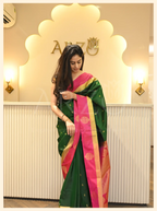 Front view of a woman wearing a handwoven dark green Mysore silk saree with a pink zari border standing inside an Arzo store.